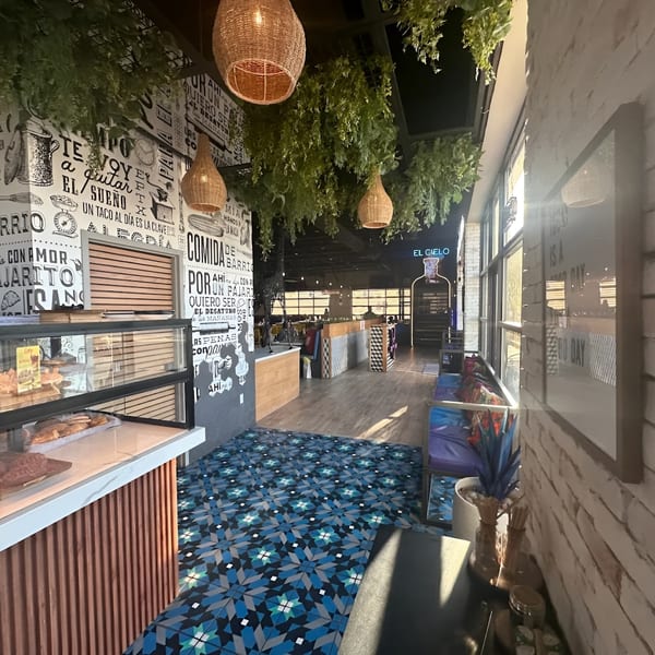 A vibrant restaurant interior with blue patterned floor tiles, a pastry display, and decorative hanging plants.