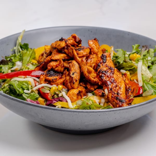 A vibrant salad with grilled chicken, mixed greens, bell peppers, corn, and pumpkin seeds in a gray bowl.