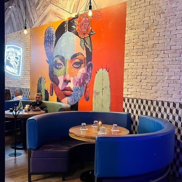 Restaurant interior with a large colorful mural of a woman's face, blue booths, and brick walls.