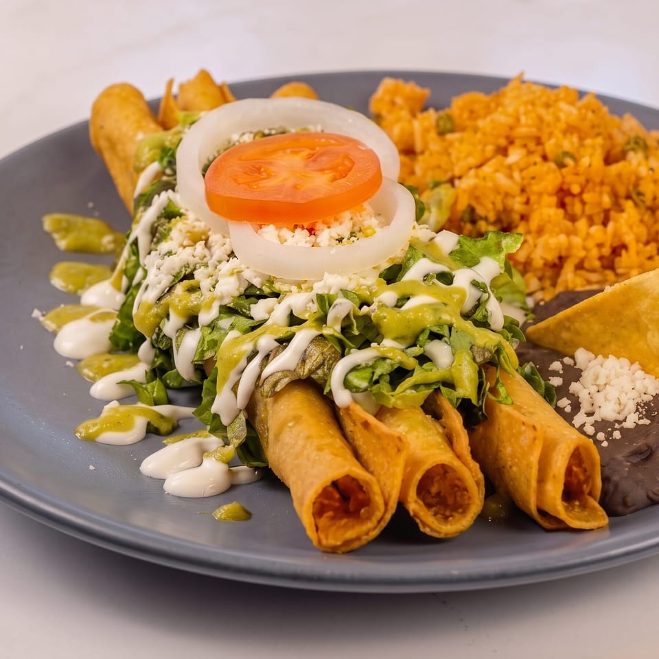 Four golden taquitos topped with lettuce, cheese, tomato, onion, and sauces, served with rice and beans.