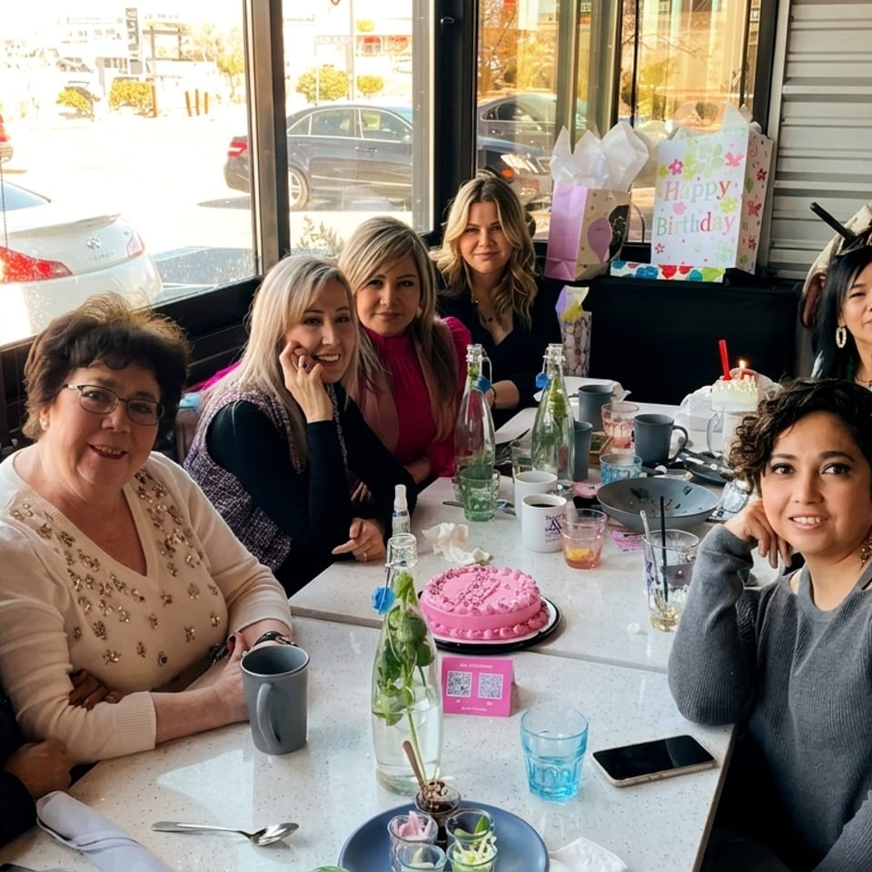 Nine women celebrating a birthday at a restaurant table with a pink cake and gifts.