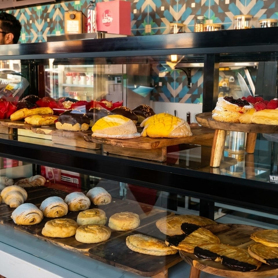 A bakery display case filled with various pastries, cakes, and breads, with a man in the background.